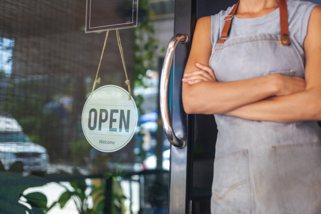 A person in an apron next to an “OPEN” sign in a window of a Birmingham business.